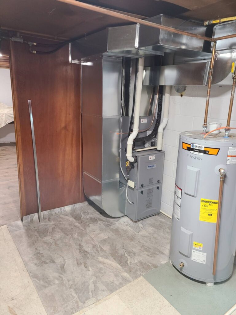 Indoor HVAC system with a furnace, ductwork, pipes, and adjacent water heater in a utility area.