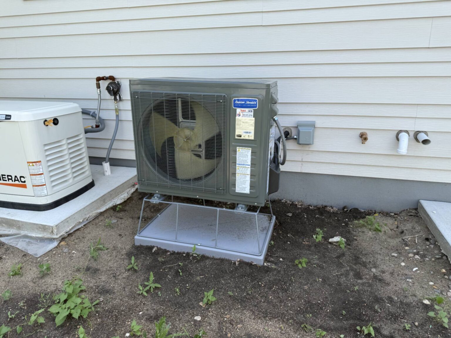 Outdoor HVAC unit mounted beside a building, with a metal protective cover and adjacent equipment.