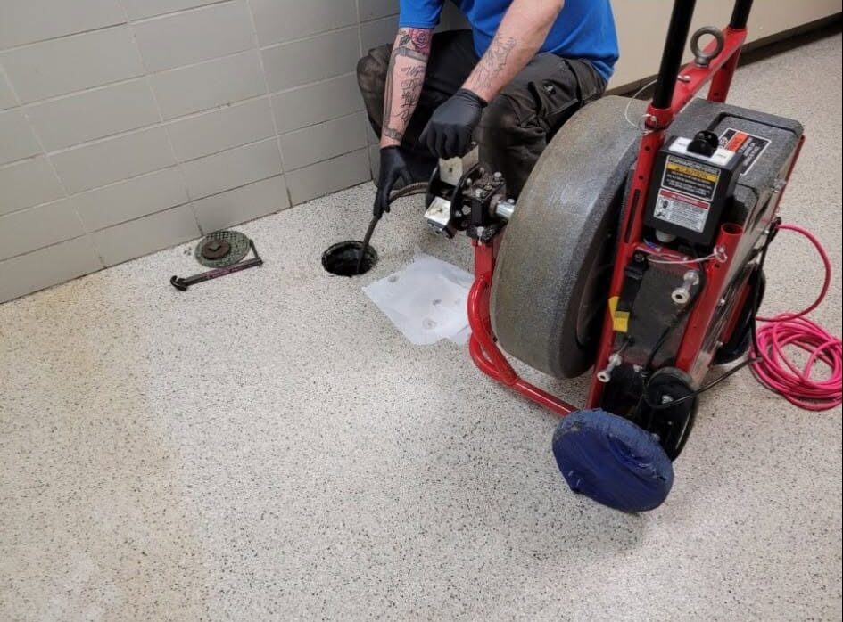 Plumber using a drain cleaning machine to clear a floor drain