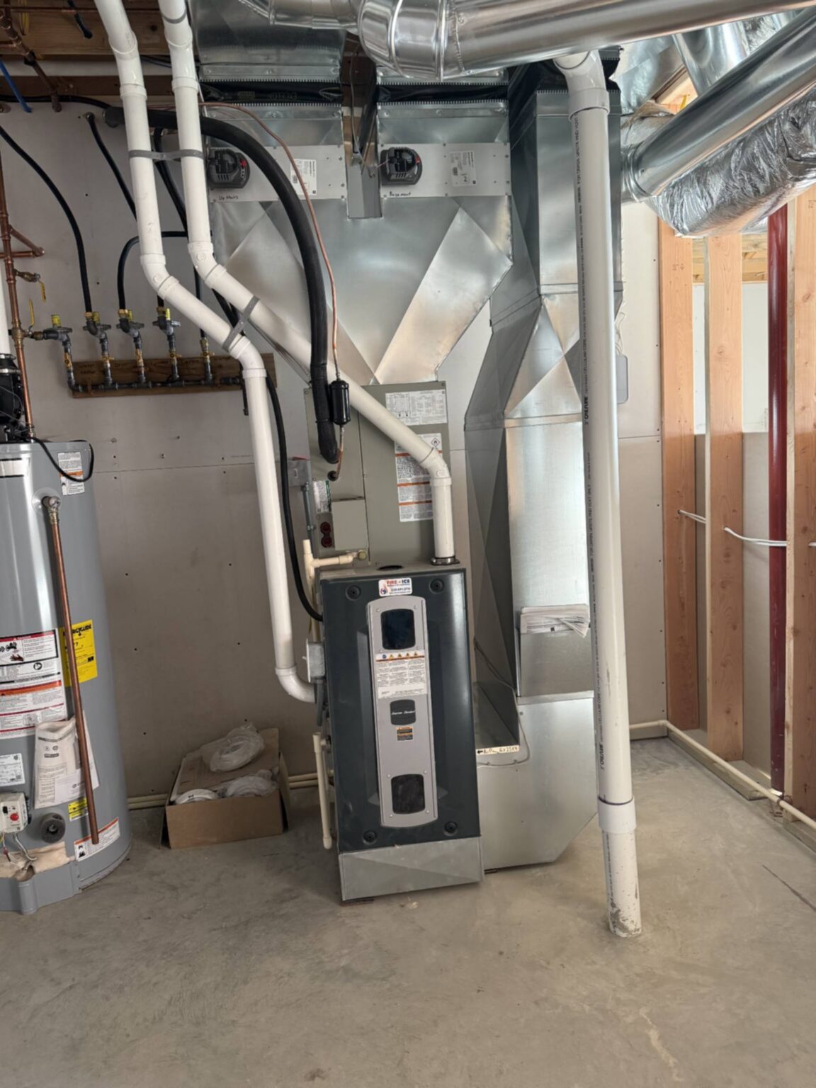 Indoor HVAC furnace with ductwork, piping, and utility connections.