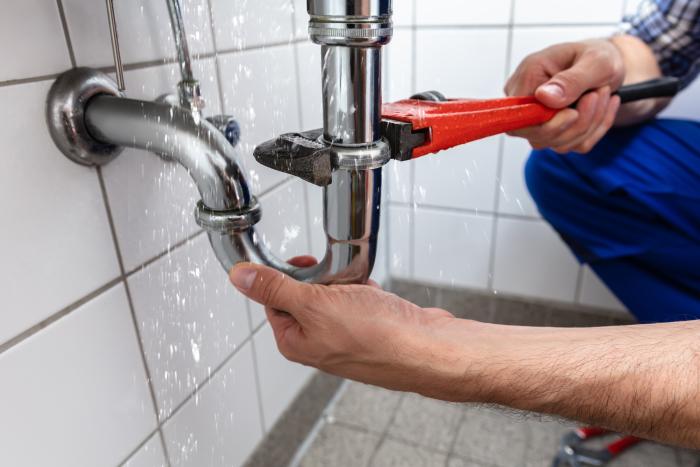 Plumber using a wrench to repair a sink drain pipe.